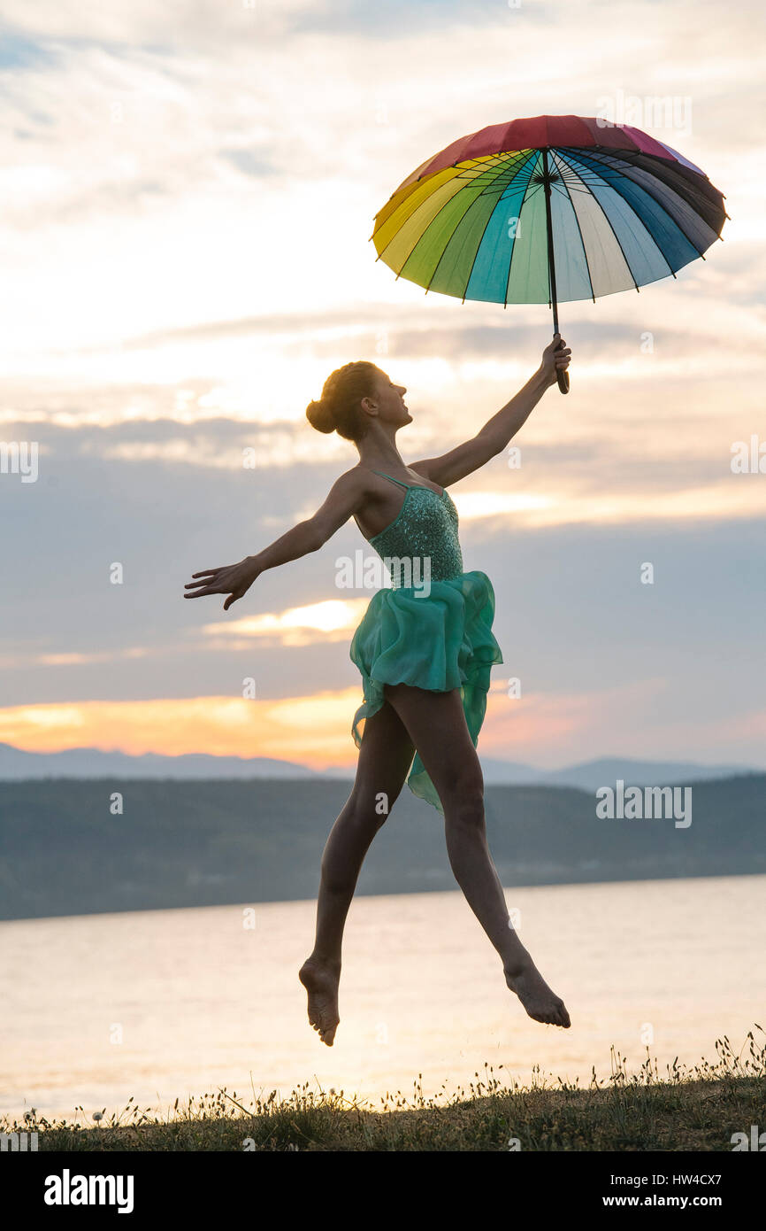 Bailarina caucásica saltando con sombrilla multicolor en la playa Foto de stock