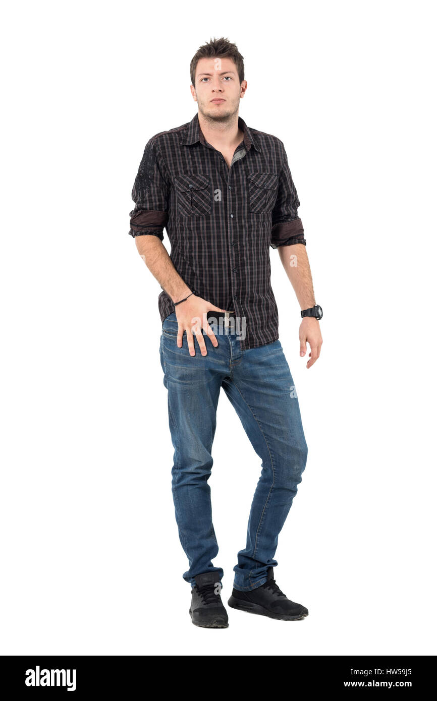 Cool machista modelo casual masculino en pantalones vaqueros y camisa de cuadros escoceses mirando a la cámara. Longitud de cuerpo completo retrato sobre fondo blanco studio. Foto de stock