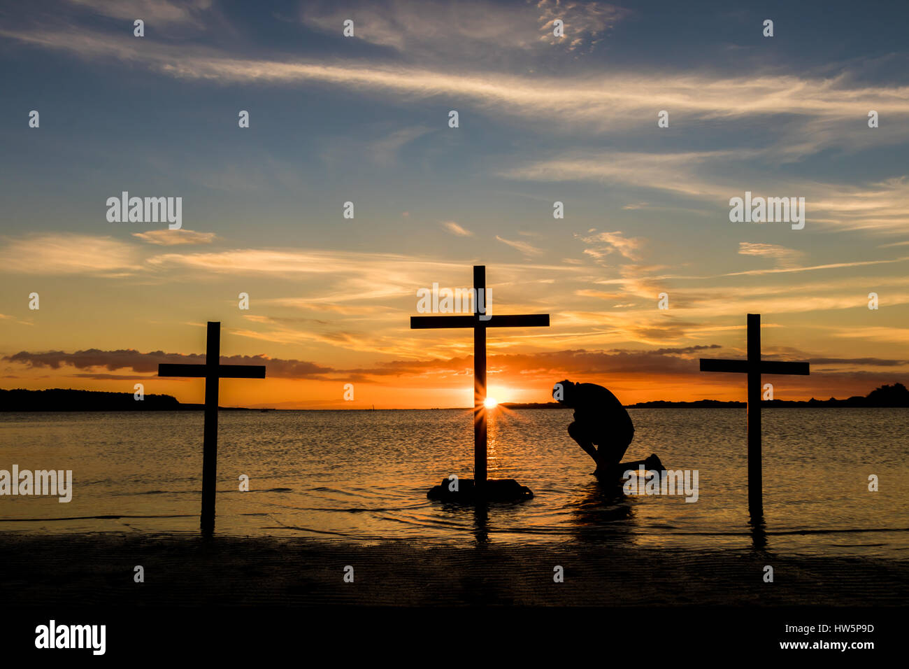 Hombre arrodillado ion oración en tres cruces al atardecer Fotografía de  stock - Alamy
