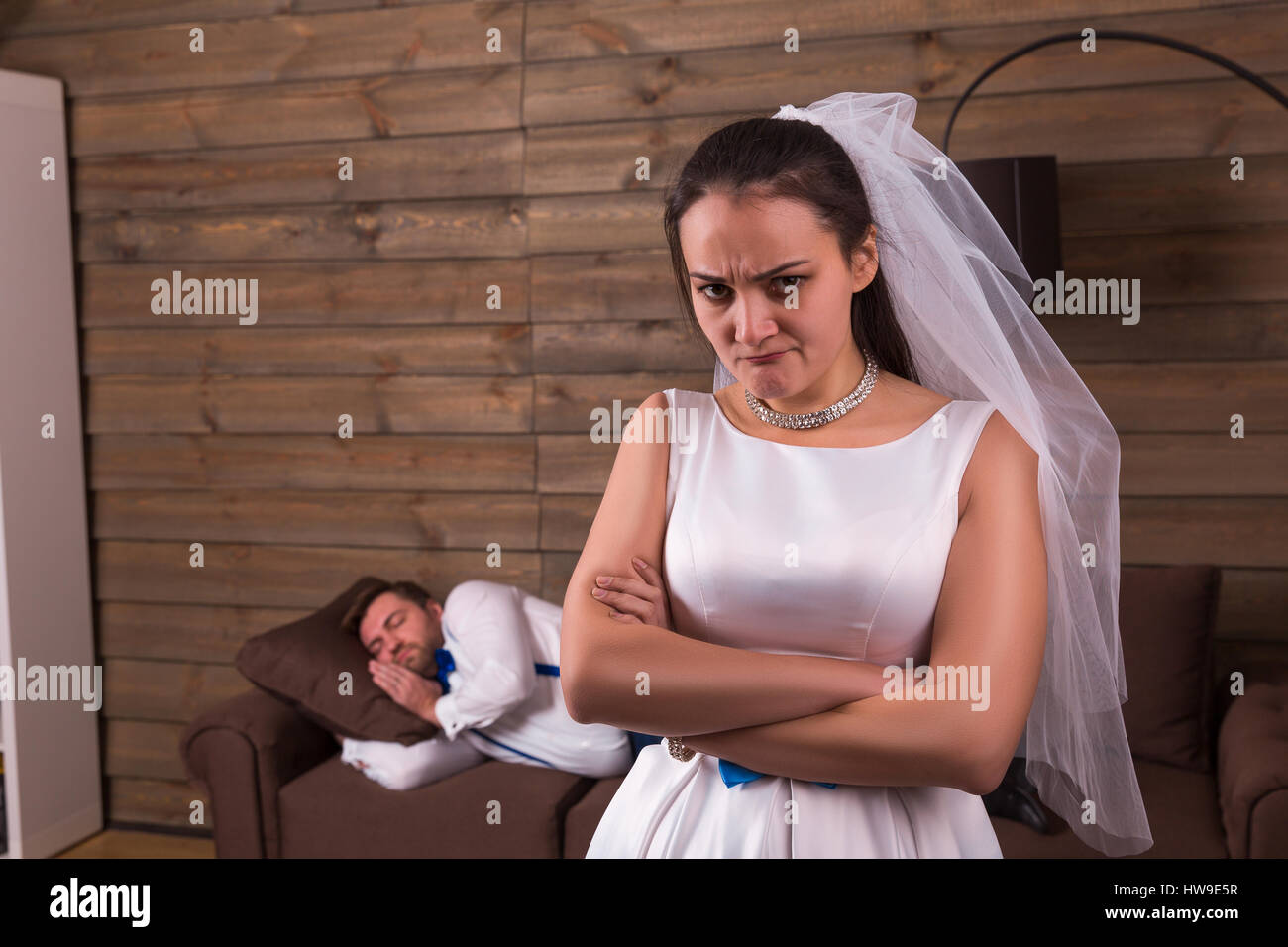 Infeliz esposa en vestido blanco y velo, durmiendo en cama el novio en el fondo. Después de la celebración de boda Foto de stock