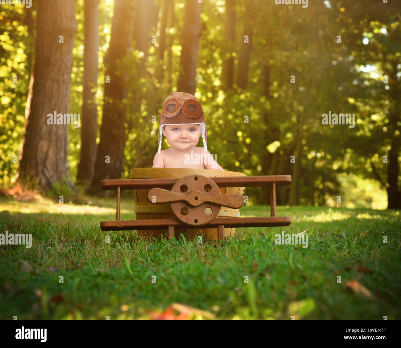 Un bebé está sentado en un avión de madera cesta prop en el parque pretendiendo viajar y volar con un piloto para un sombrero sobre creatividad o imaginación Foto de stock
