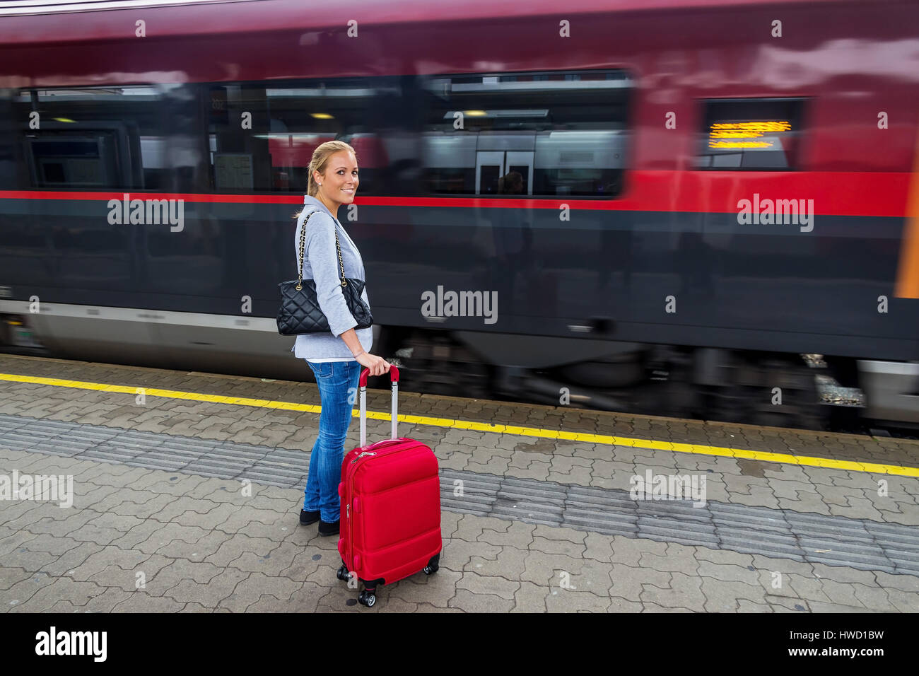 Una joven mujer espera un tren en una estación ferroviaria. Viaje en tren en las vacaciones, Eine junge Frau wartet auf einen Zug en einem Bahnhof. Zugfahrt Foto de stock