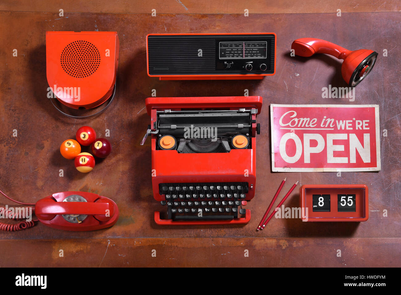Ángulo alto todavía la vida de la colección de objetos de color rojo sobre el mostrador de madera - el altavoz, radio, máquina de escribir, signo abierto, reloj, lápices, teléfono, piscina de bolas y Mic Foto de stock