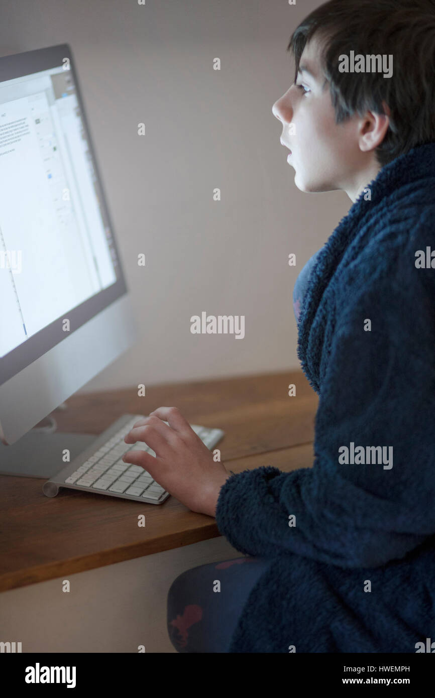 Chico en bata escribiendo en el ordenador en casa Foto de stock