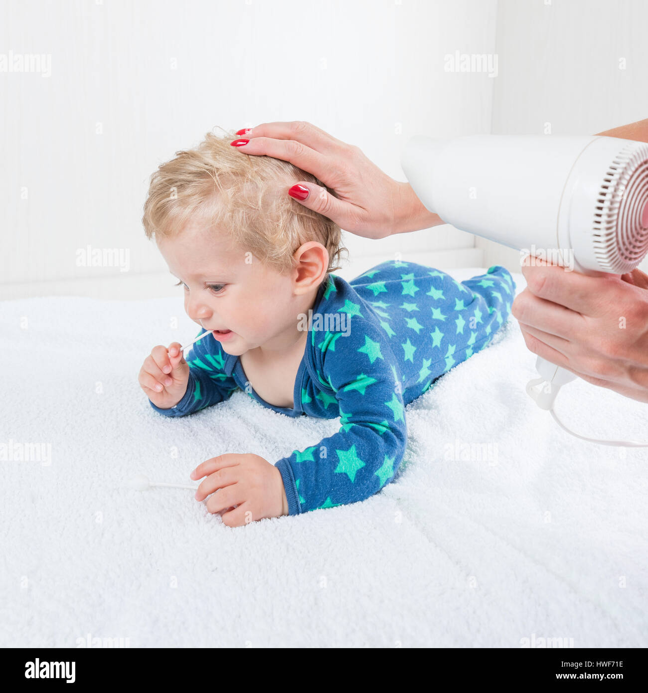 Mamá se seca Baby Boy el cabello con un secador seca, mientras que los  juguetes acostado con hisopo de algodón Fotografía de stock - Alamy