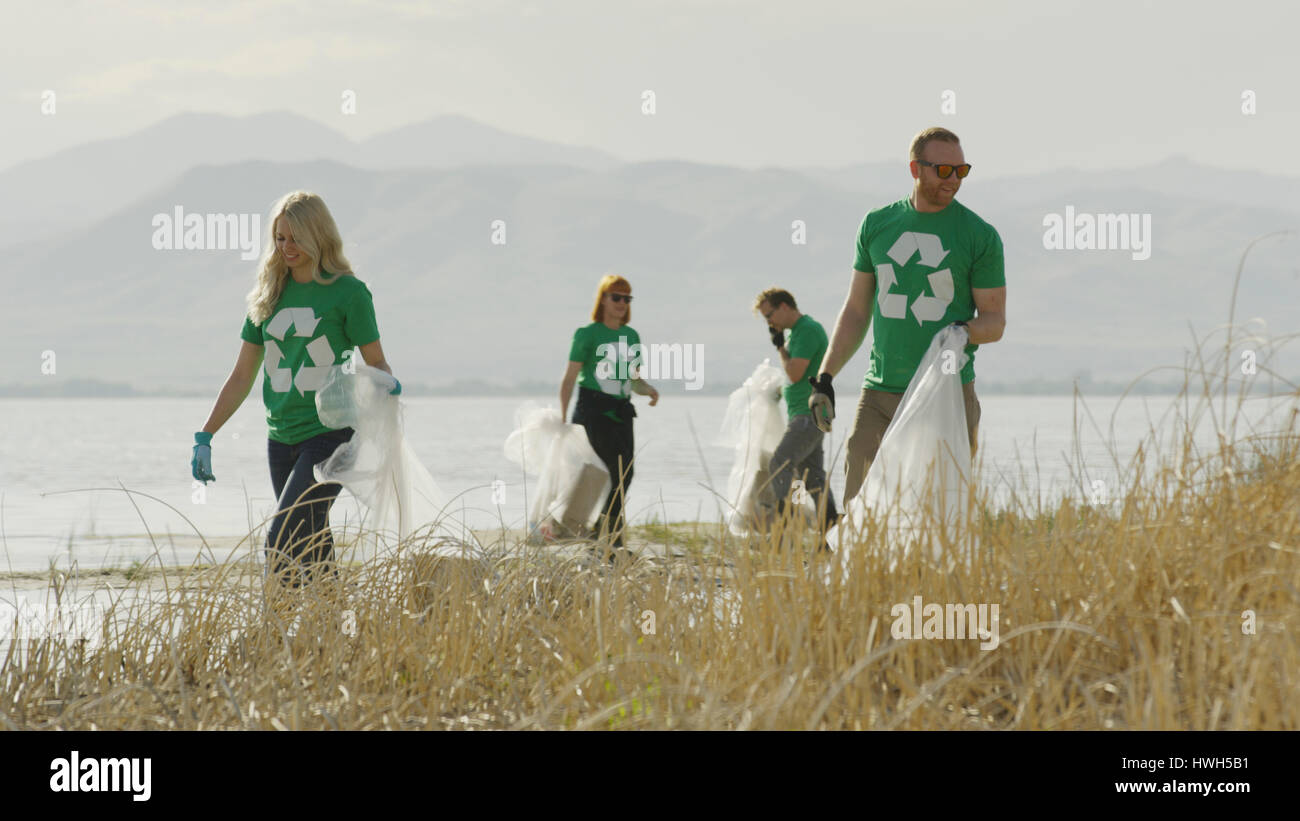 Los voluntarios recogiendo basura y reciclaje de basura en la orilla del lago de hierba remota Foto de stock
