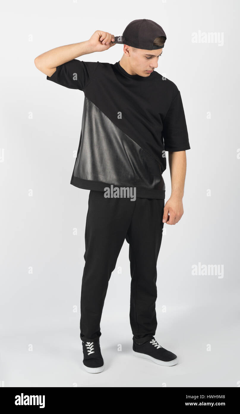 Musculoso joven hombre vestido con ropa negra y zapatillas aislado sobre  fondo blanco. Él está sosteniendo y snapback mirando hacia abajo Fotografía  de stock - Alamy