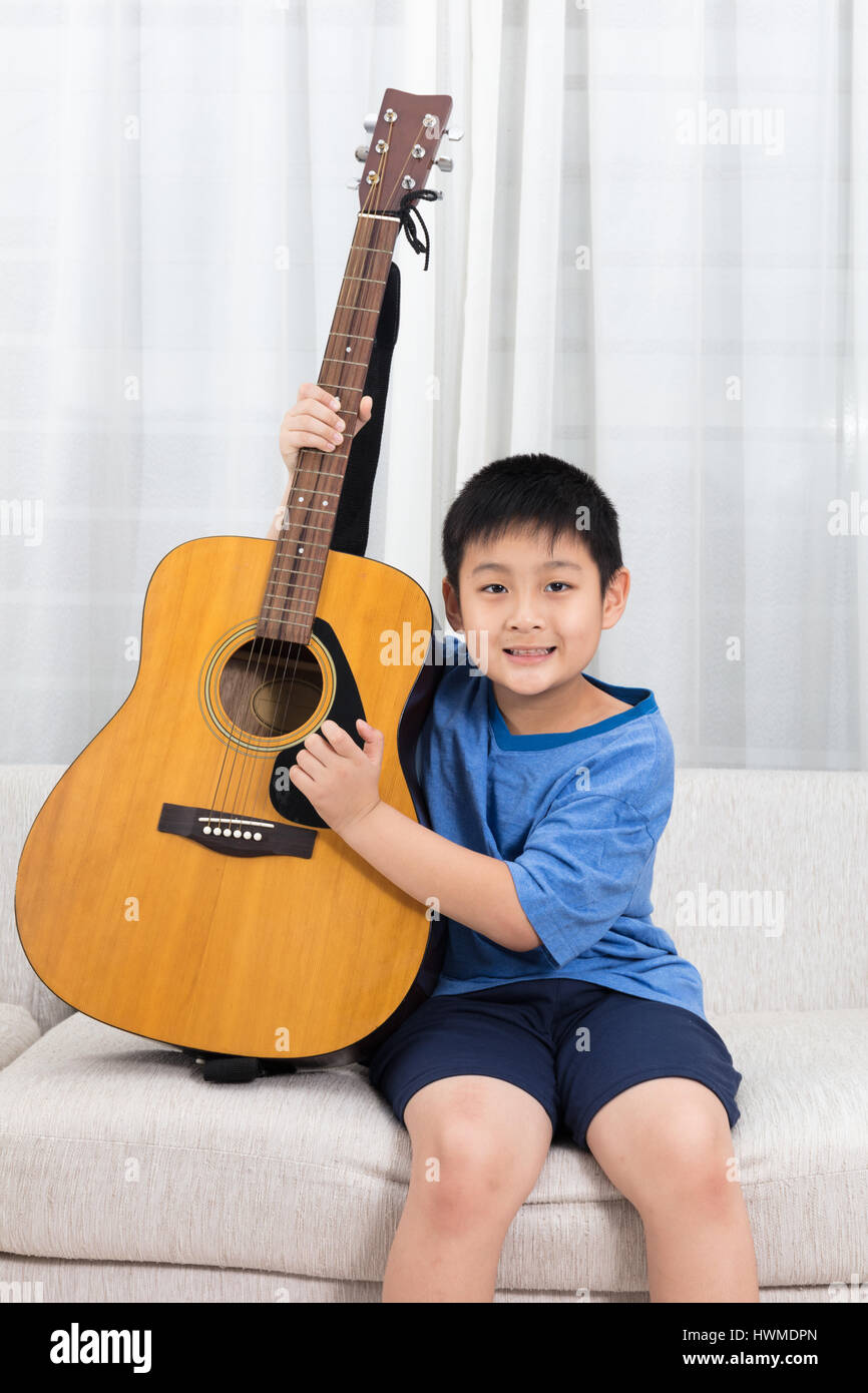 Feliz chino asiático chico tocando la guitarra en el sofá en el salón de  casa Fotografía de stock - Alamy