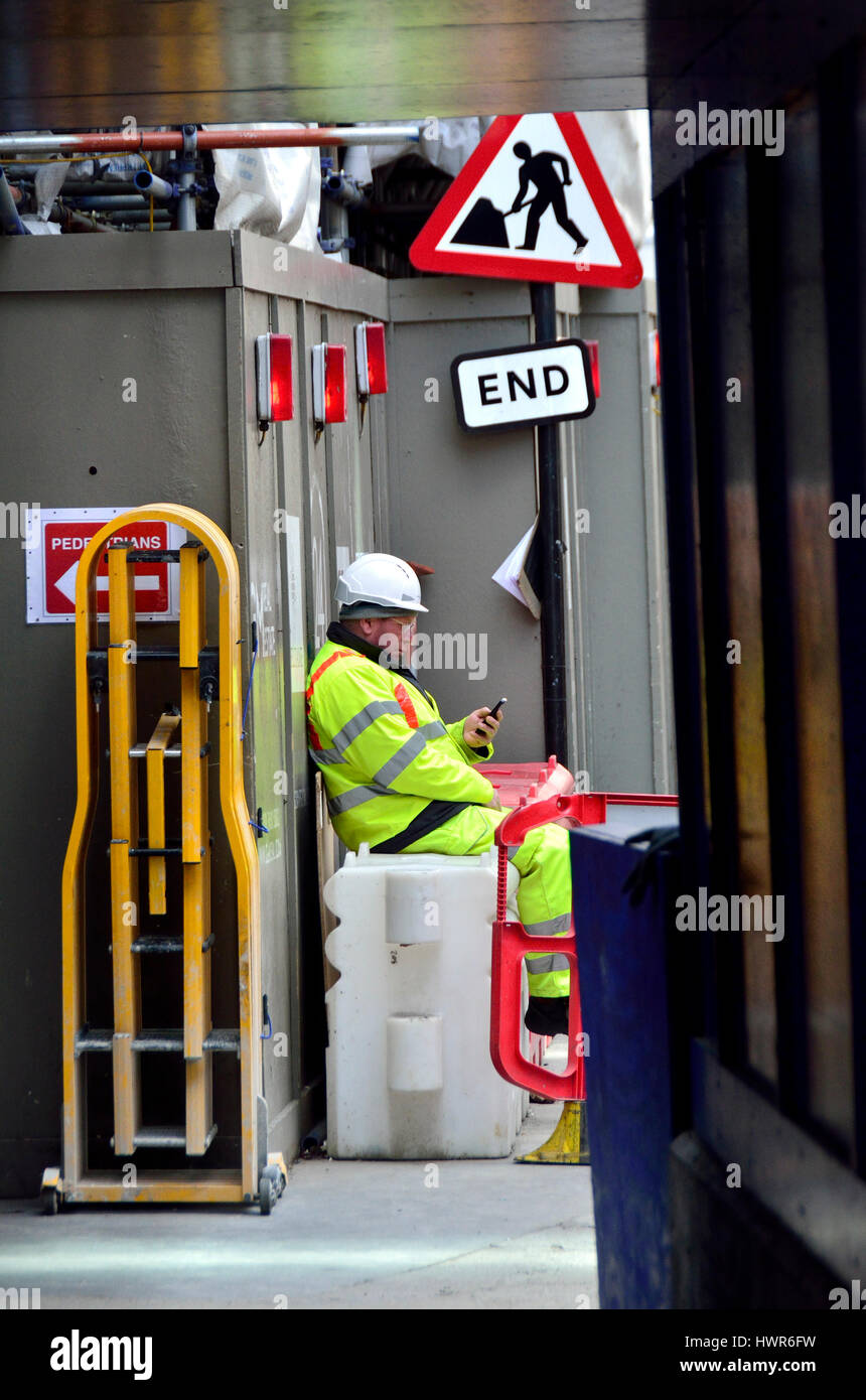 Londres, Inglaterra, Reino Unido. Trabajador de la construcción, tomando un descanso en su teléfono móvil Foto de stock
