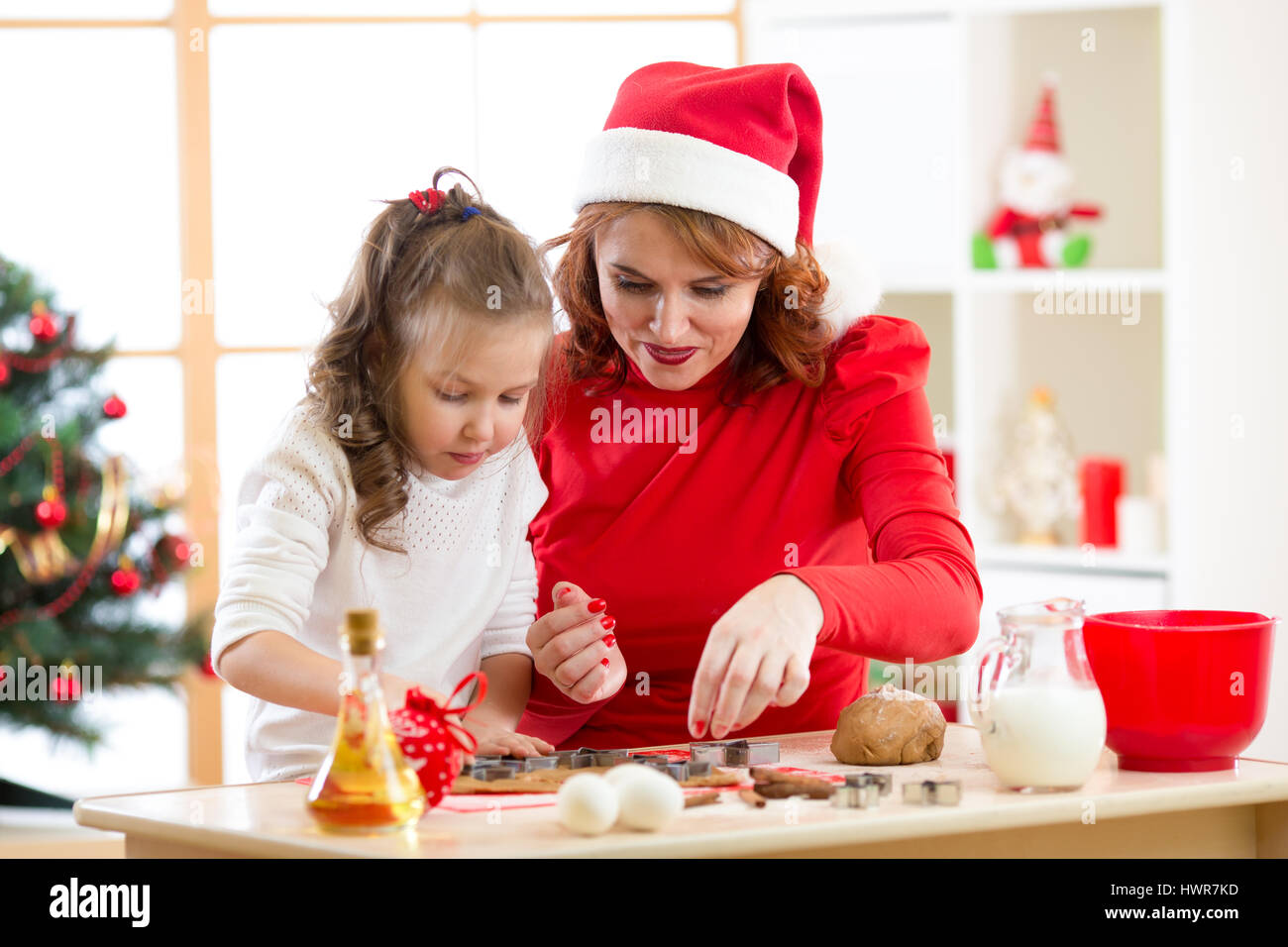 Niño feliz chica y la madre de X-mas para hornear galletas juntos en la habitación de decoración navideña Foto de stock