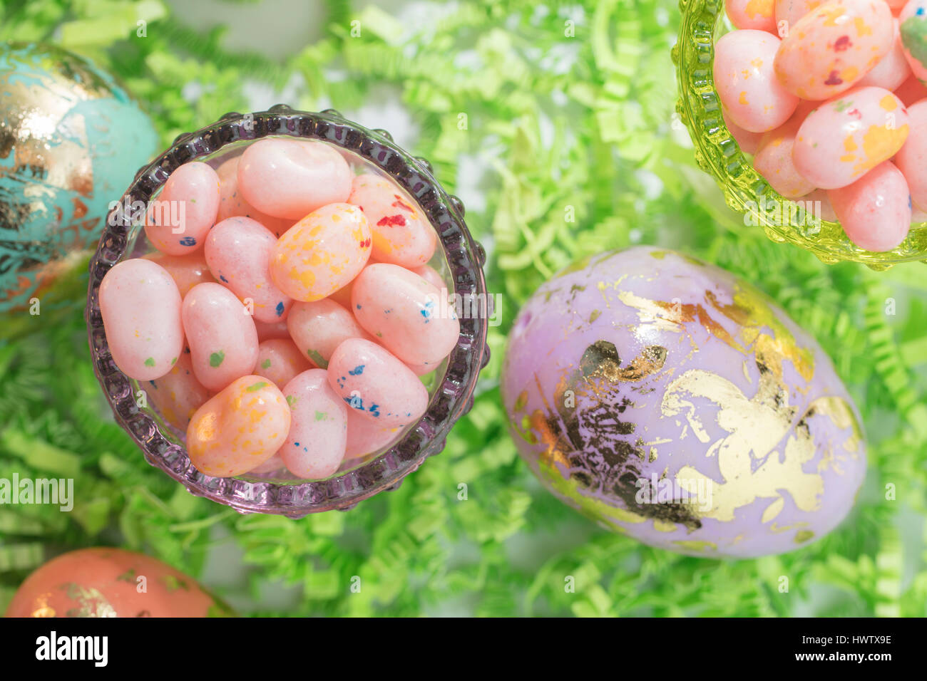 Los huevos de Pascua y Jelly Beans en un recipiente de vidrio y de papel crepé verde Foto de stock