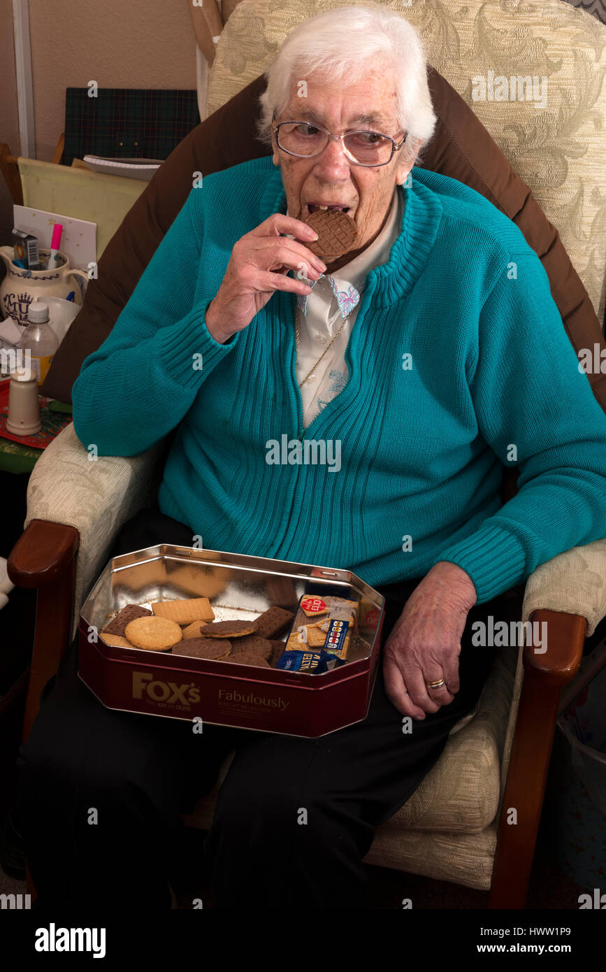 Están confinadas en sus hogares anciana comiendo una galleta de chocolate Foto de stock