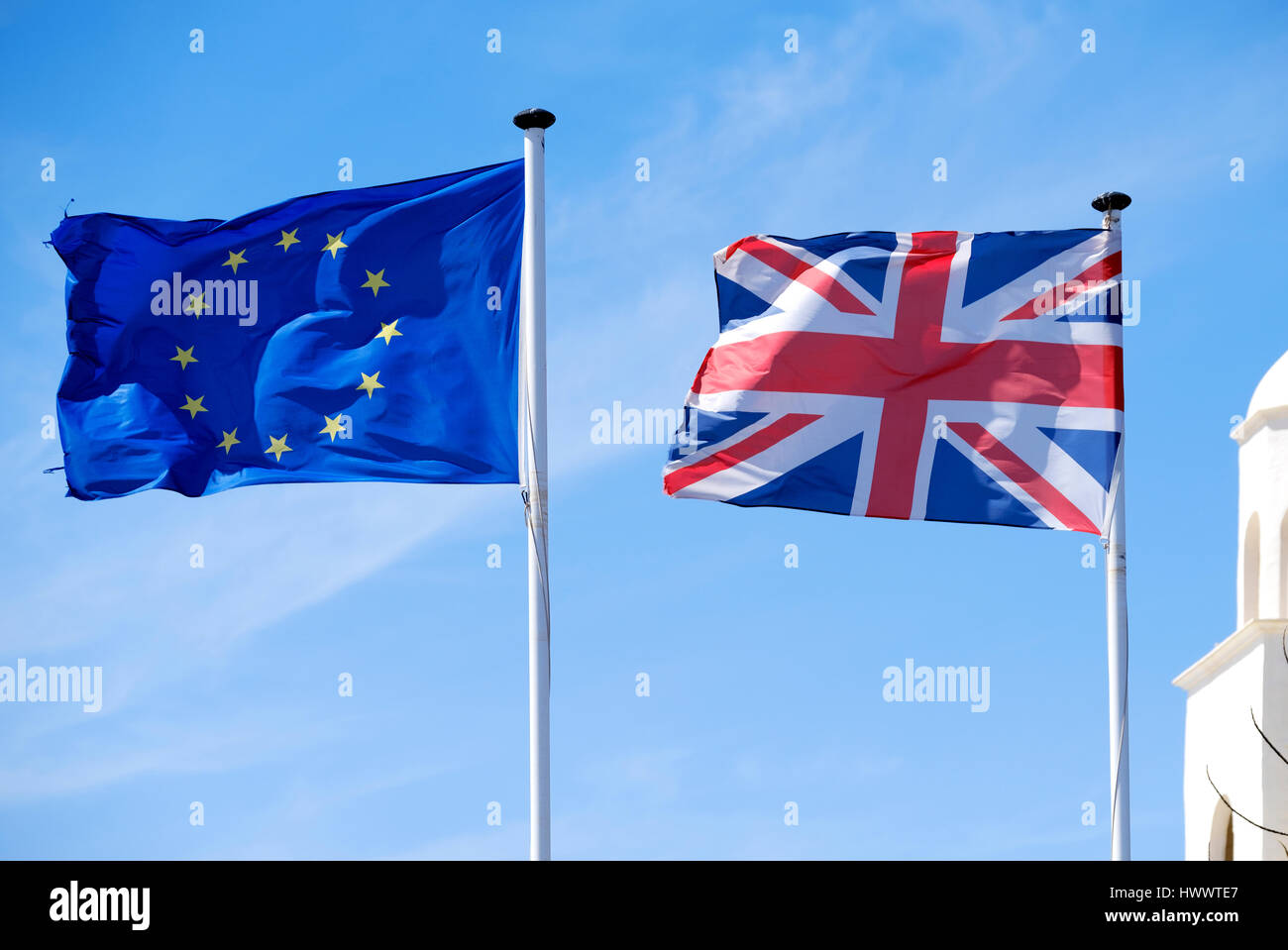 Una bandera Union Jack junto una bandera europea o la bandera de Europa. Ambos soplando ferozmente en una brisa fuerte contra un fondo de cielo azul Foto de stock