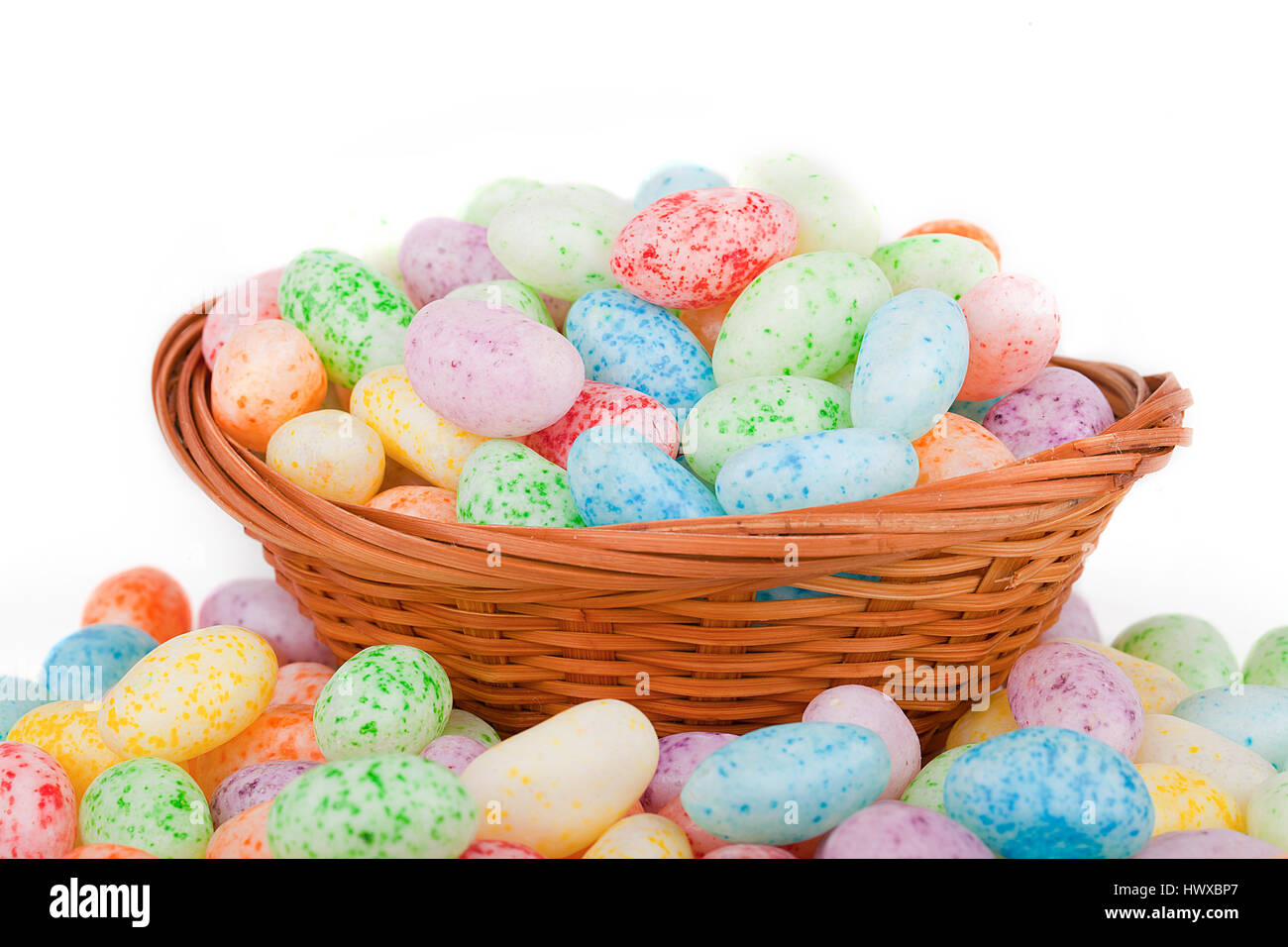 Coloridos huevos de Pascua en una cesta de mimbre sobre la superficie blanca. La Pascua Jelly Beans aislado en blanco. Foto de stock