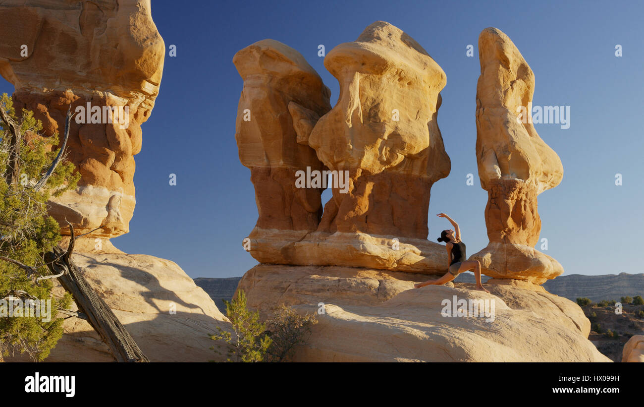 Ángulo de visión baja de mujer practicando yoga y meditación de formaciones rocosas en el remoto desierto paisaje bajo el cielo azul claro Foto de stock