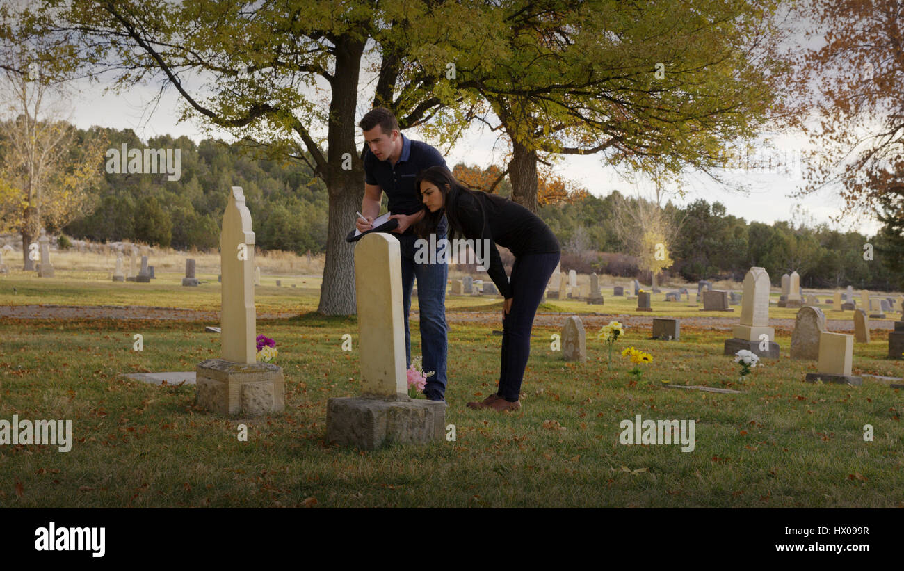 Novio y novia examinar tumba en el cementerio solitario Foto de stock