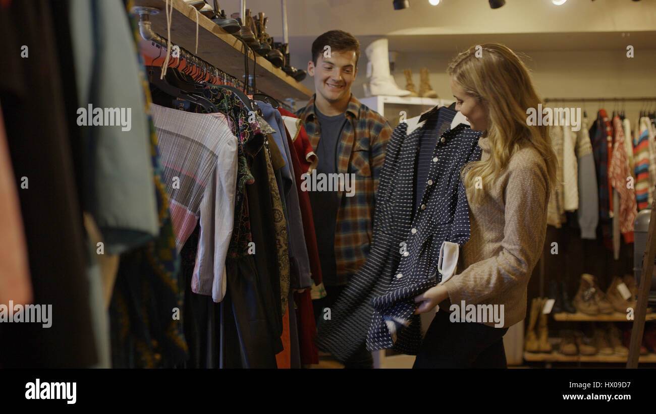 Ángulo de visión baja de novio y novia admirando la ropa en la tienda de moda Foto de stock