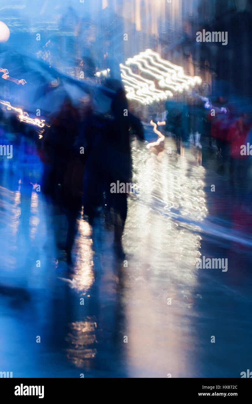 Resumen Antecedentes En naturale en tonos azules. La gente caminando por las calles de la ciudad en la lluviosa noche. Desenfoque de movimiento intencional. Concepto de las estaciones, el clima, la ciudad moderna. Foto de stock