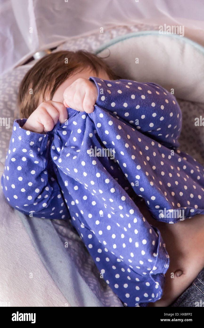 Hace tres meses bebé niña jugando peek-a-boo usando su camisa para cubrir sus ojos Foto de stock