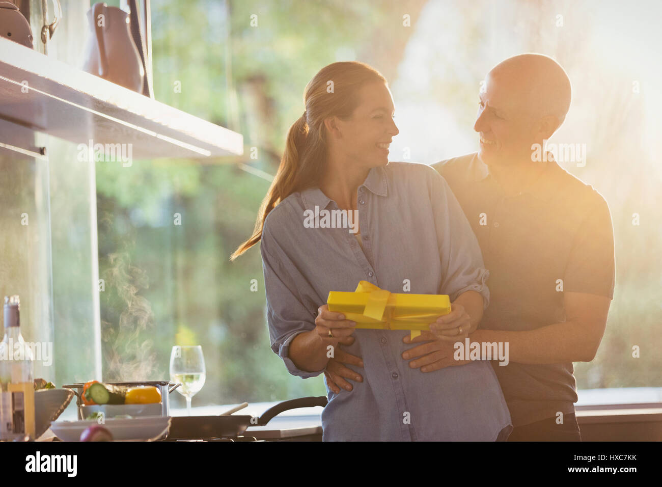 Sonriente marido sorprendente esposa con don en la soleada cocina Foto de stock