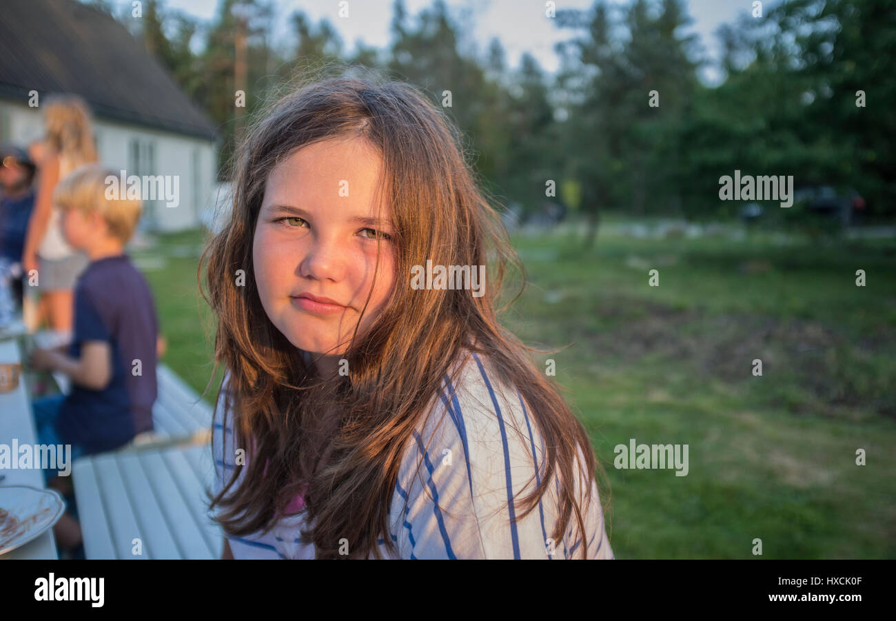 Retrato de una niña mirando a la cámara en una mesa de comer fuera en el jardín. Foto de stock
