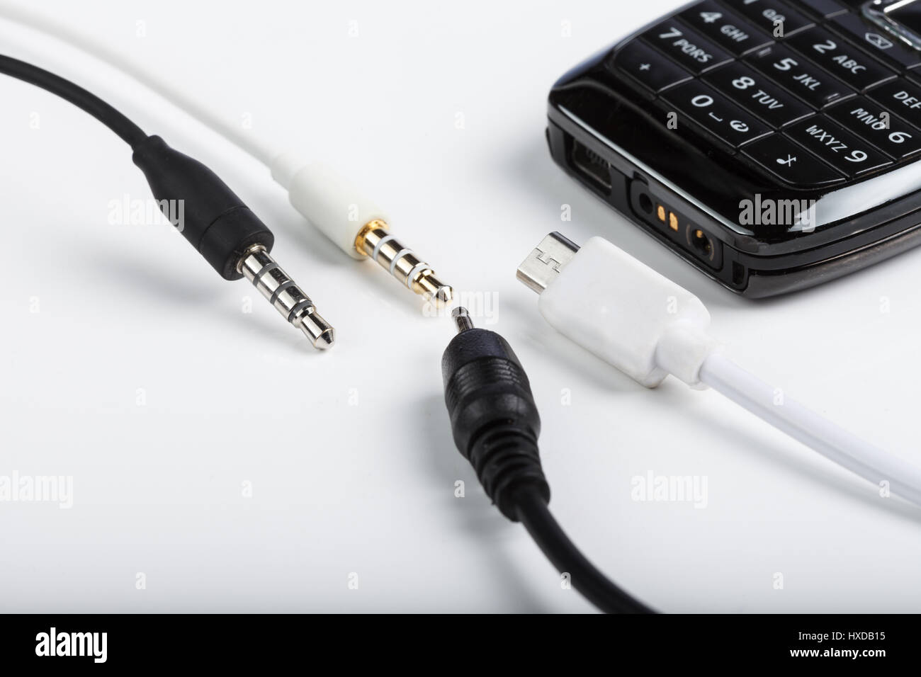 Accesorios de telefonía celular móvil, enchufe los auriculares, conectores aislados en un fondo blanco con un negro teléfono con teclado Foto de stock