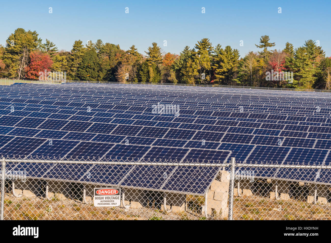 Paneles solares en un campo con señal de alta tensión Foto de stock