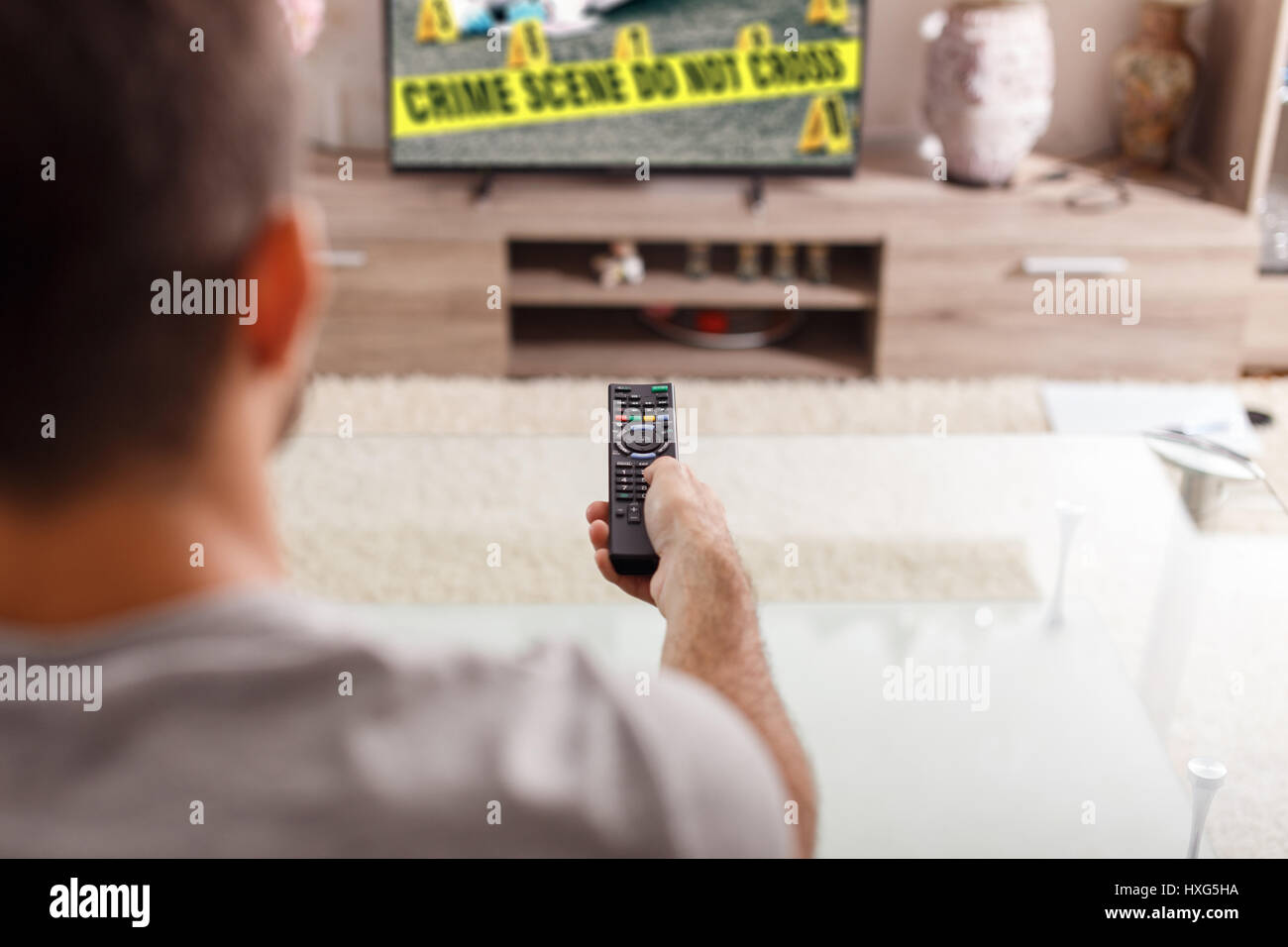 Hombre con control remoto viendo crimen serie en TV en casa Foto de stock