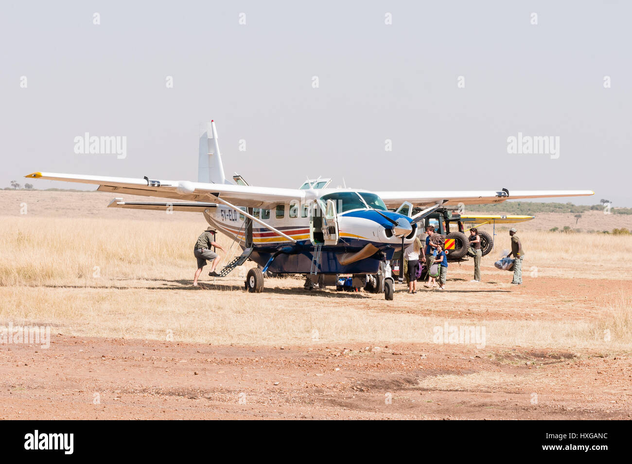 Avión Cessna esperando en pista polvorienta, mientras que los pasajeros de aviones de carga, Maasai Mara Foto de stock