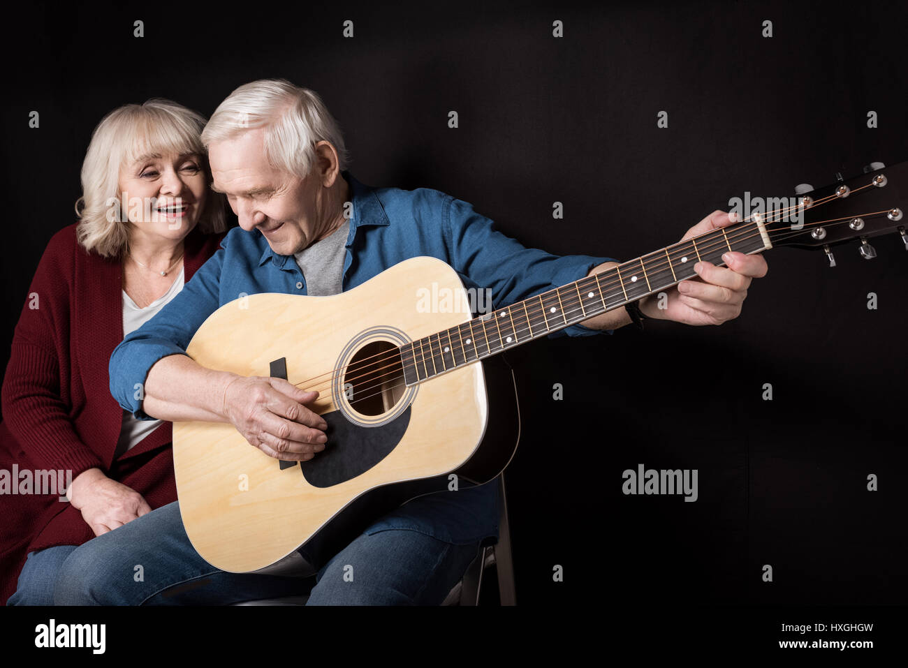 Vista lateral del hombre senior tocando la guitarra con su esposa cerca por sobre negro Foto de stock