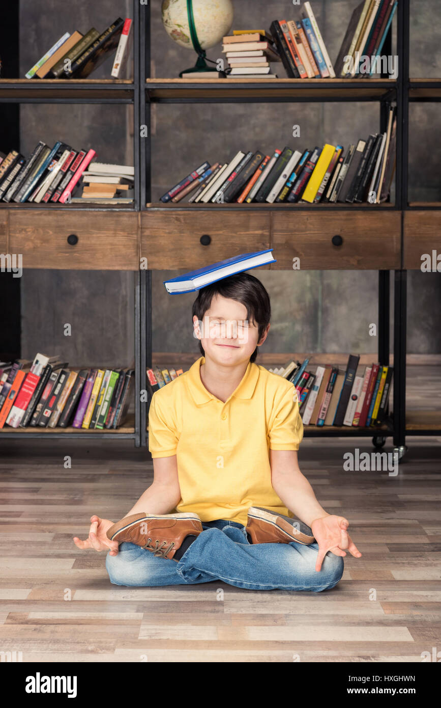 Chico sonriente con el libro en la cabeza sentado en lotus plantean en la  biblioteca Fotografía de stock - Alamy