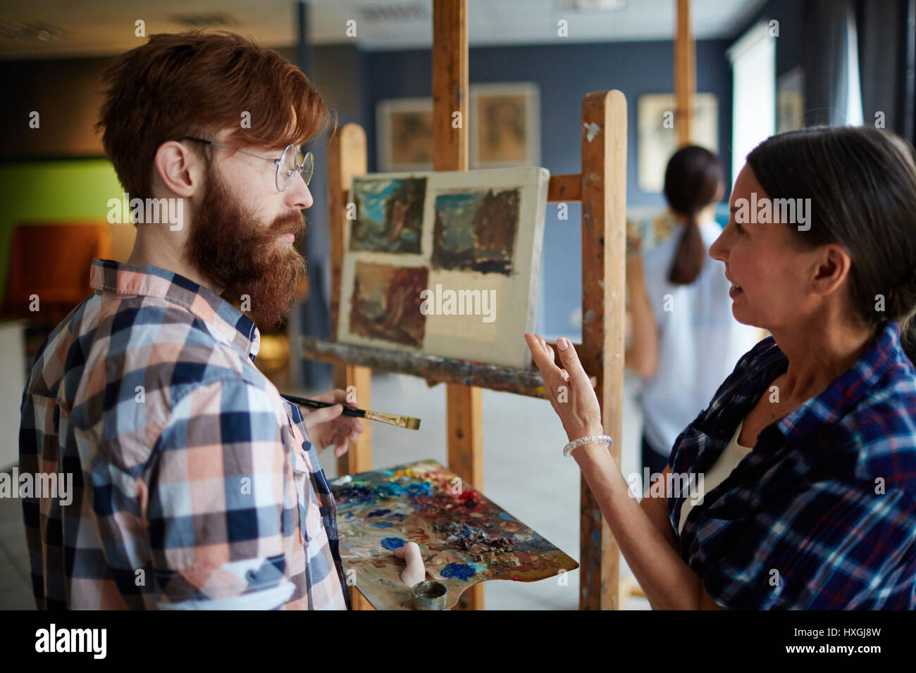 Profesor experimentado consulta a su estudiante y apuntando a su pintura Foto de stock