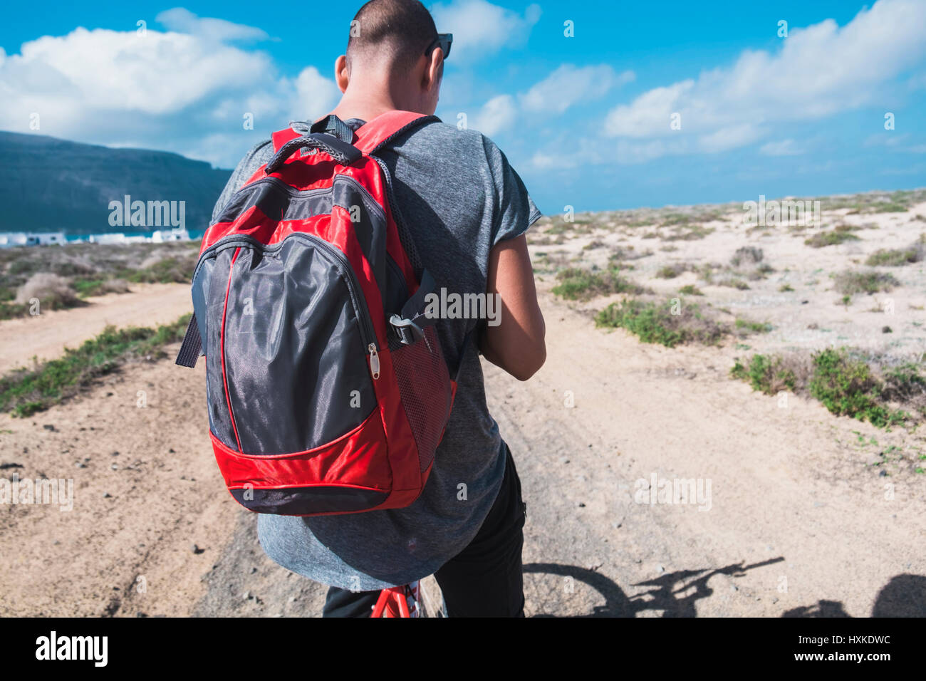 Un hombre joven con una mochila visto desde una moto, se detuvo a mirar a  su smartphone o GPS, en una sucia carretera en La Graciosa, Islas Canarias,  España Fotografía de stock -