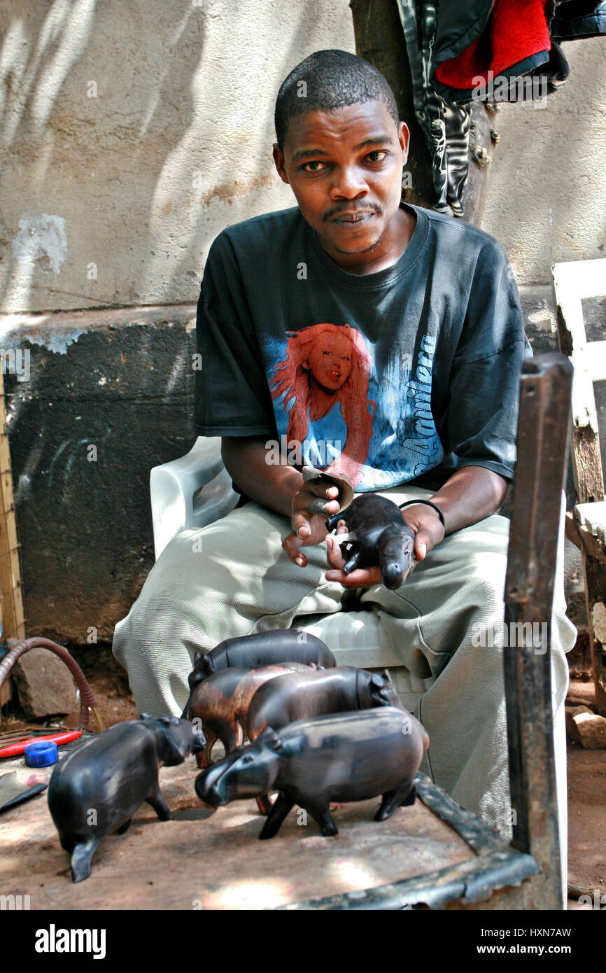 Namanga, Tanzania - Febrero 9, 2008: el joven hombre negro africano, un tallista de madera, taller de arte. Maestro de piel oscura tallados en madera, madera de pulido Foto de stock