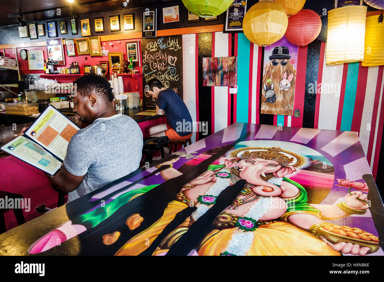 Orlando Florida, Pom Pom's Teahouse & Sandwicheria, cafetería, cafetería, mostrador, decoración, hombre negro hombres, sentado, menú de lectura, mesa pintada, Ganesha, Ganapat Foto de stock