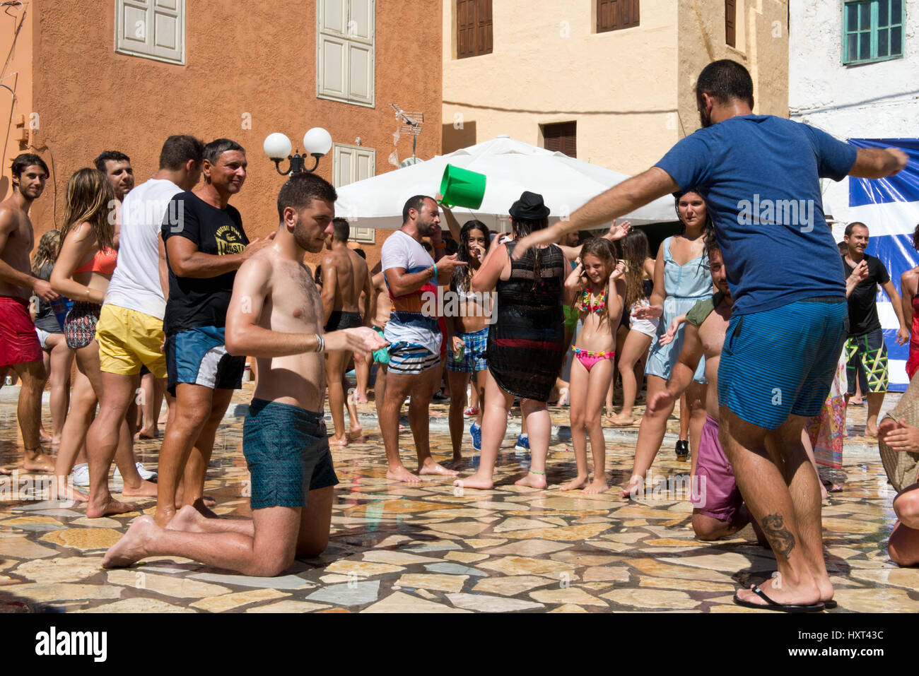 En Badekleidung tanzende Menschen auf Dorfplatz, dahinter farbige Häuser und griechische Fahne, Insel, Kastellorizo Dodekanes, Griechenland Foto de stock
