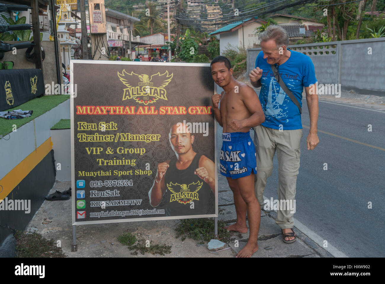 Kru Sak, un boxeador o tailandés Muay Thai, posa junto a un cartel ofrece su gimnasio mientras que un turista occidental se une en Phuket, Tailandia. 09-Mar-2017 Foto de stock