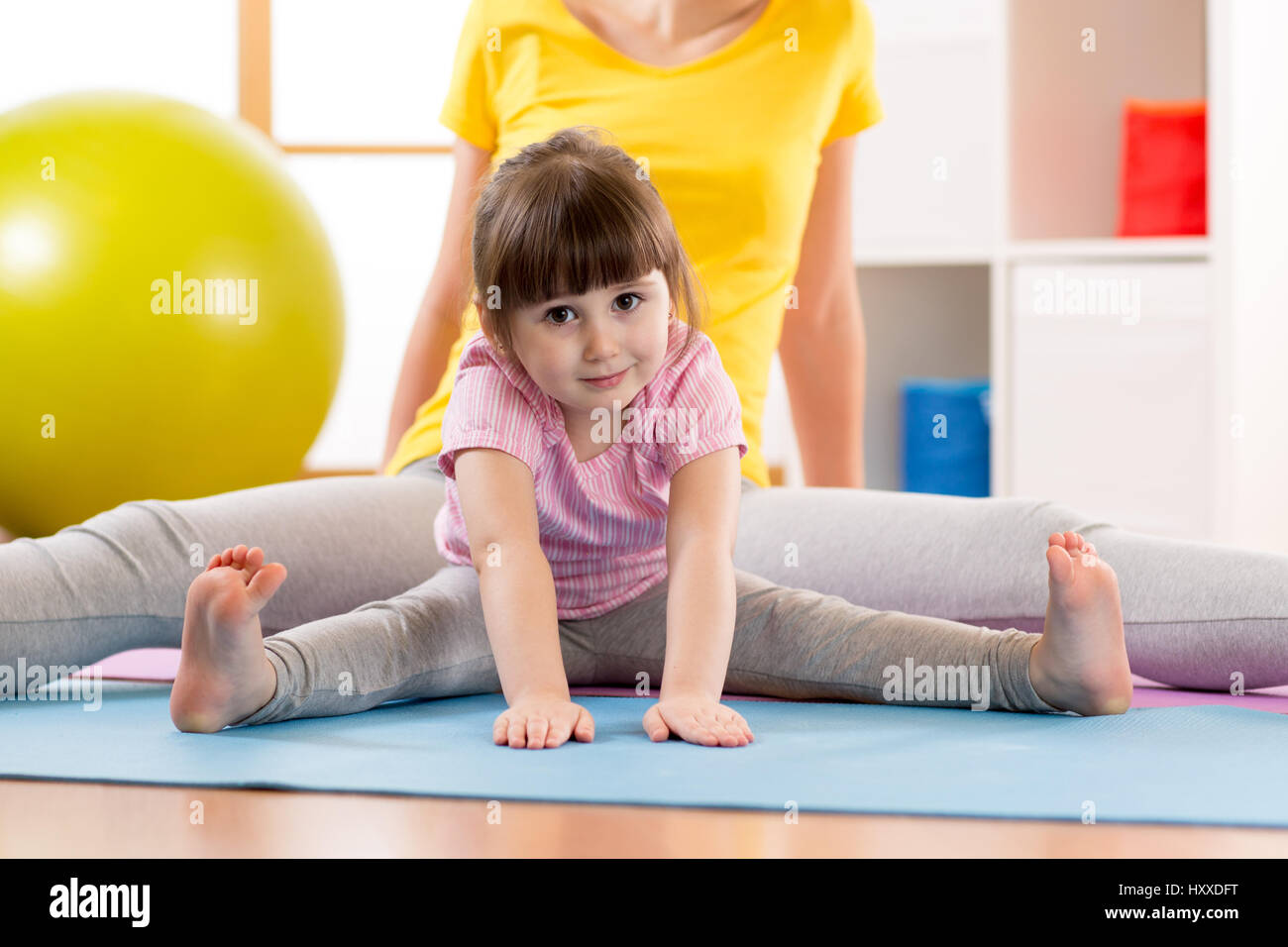 Madre e hija kid haciendo ejercicios deportivos. Niño doblado hacia abajo estirando con las manos al suelo. Foto de stock