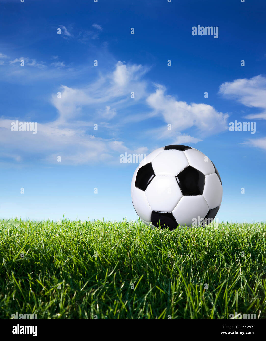 Ángulo de visión baja de un balón de fútbol en hierba contra el cielo azul y las nubes Foto de stock