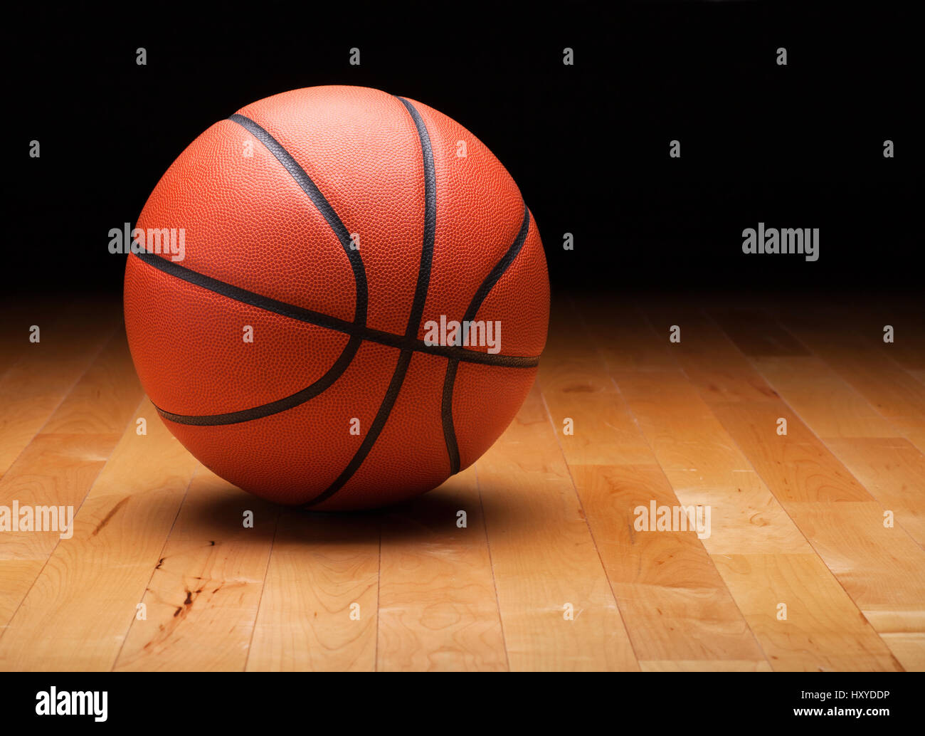 Un baloncesto con un fondo oscuro en un gimnasio de piso de madera Foto de stock