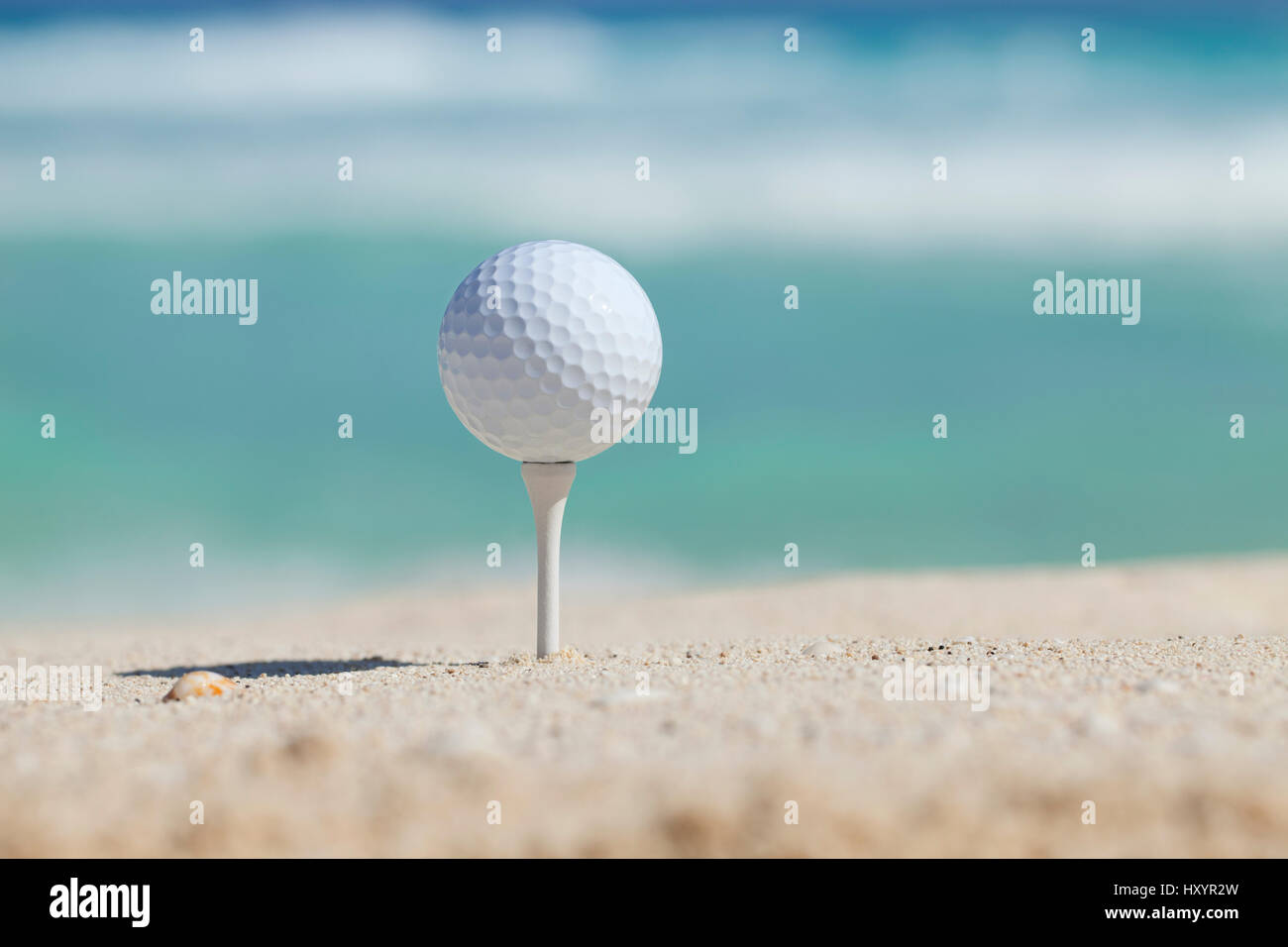 Pelota de golf blanca en t en la arena de la playa con las olas del océano de enfoque suave detrás Foto de stock