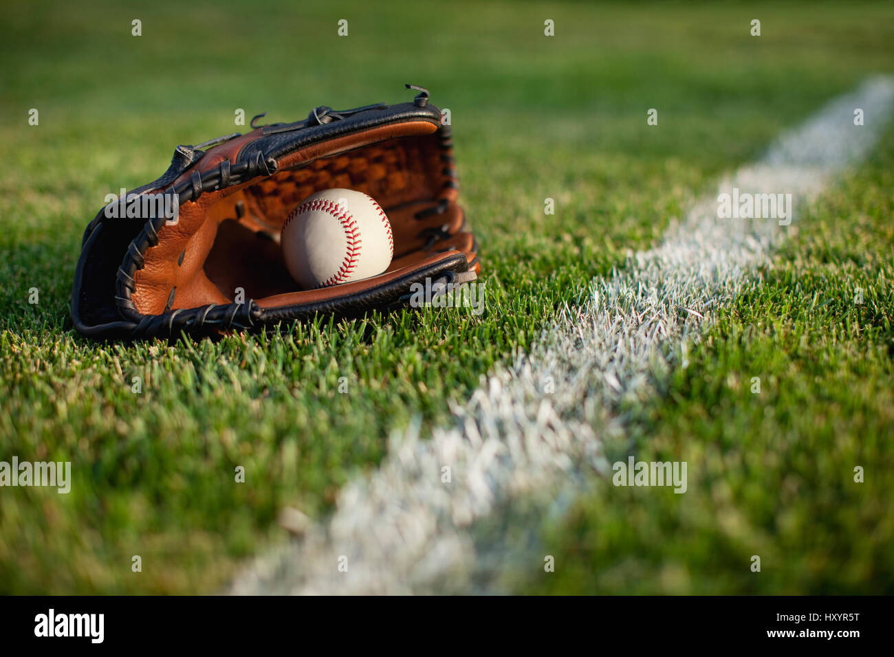 Un enfoque selectivo, ángulo de visión baja de un guante de béisbol y la pelota en el césped por una franja de campo Foto de stock