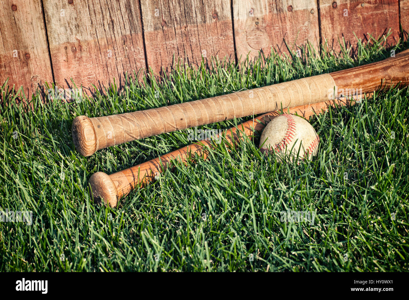 Vintage bates de béisbol y tumbados en la hierba delante de una vieja valla Foto de stock