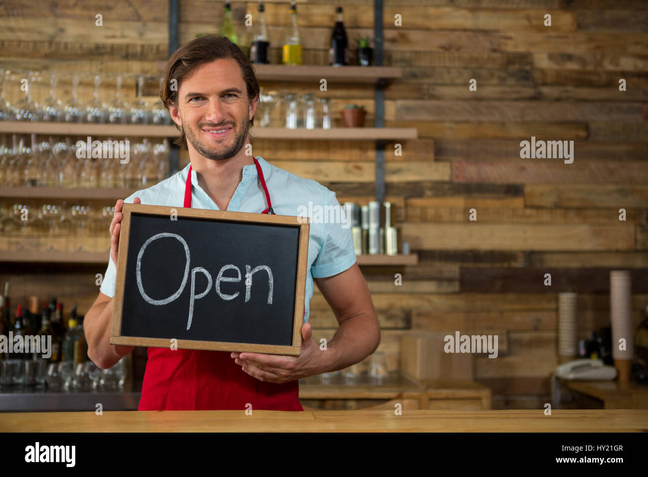 Retrato de barista macho feliz celebración abrir cartel en la cafetería. Foto de stock