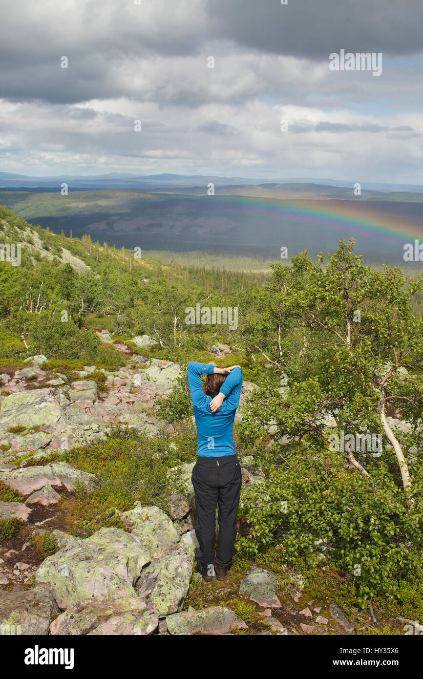 Suecia, Dalarna Fulufjallet, hombre de pie en la colina y mirando el paisaje con arco iris Foto de stock