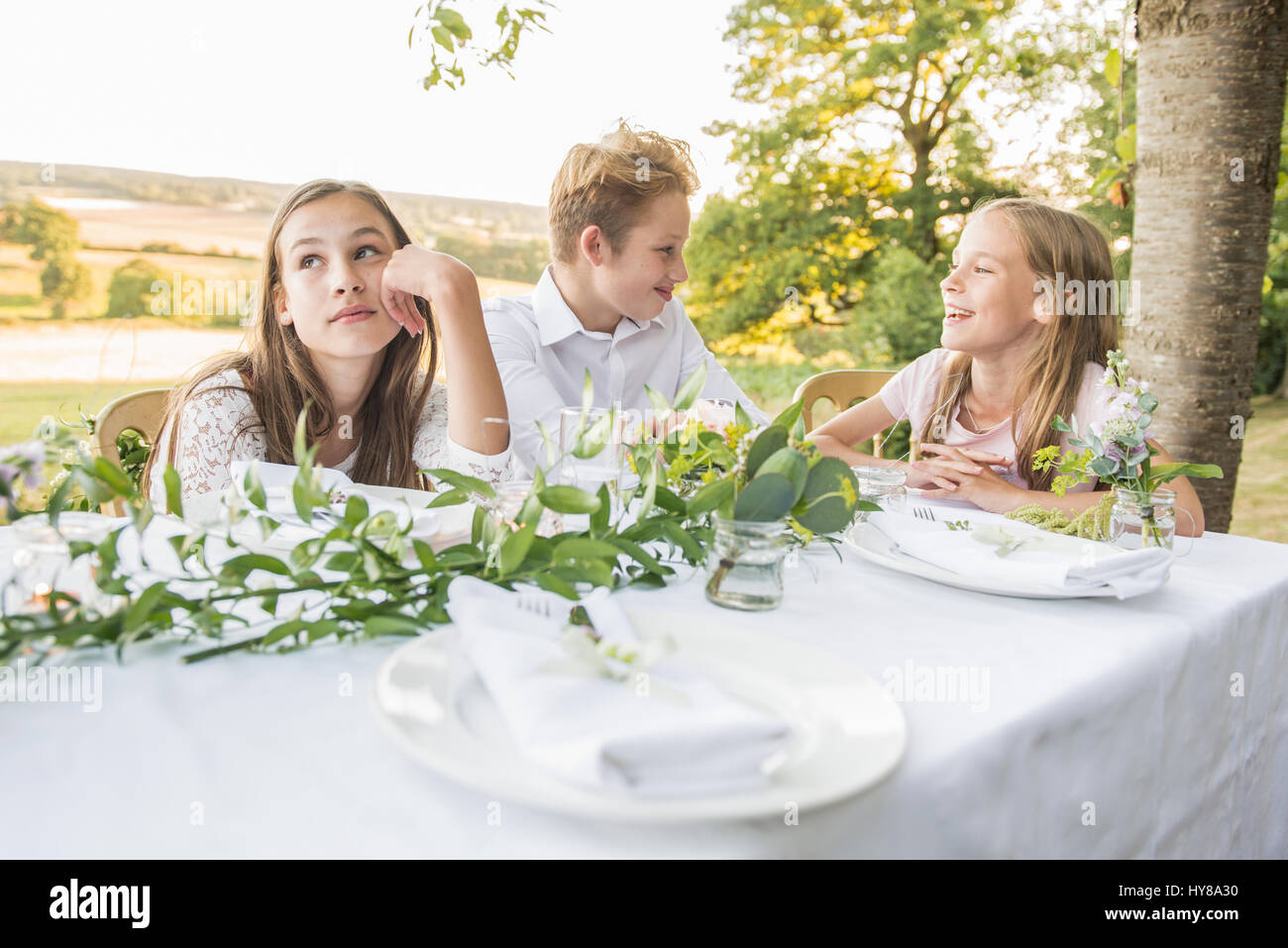 Los niños sentados en la mesa de la cena fuera en el sol Foto de stock
