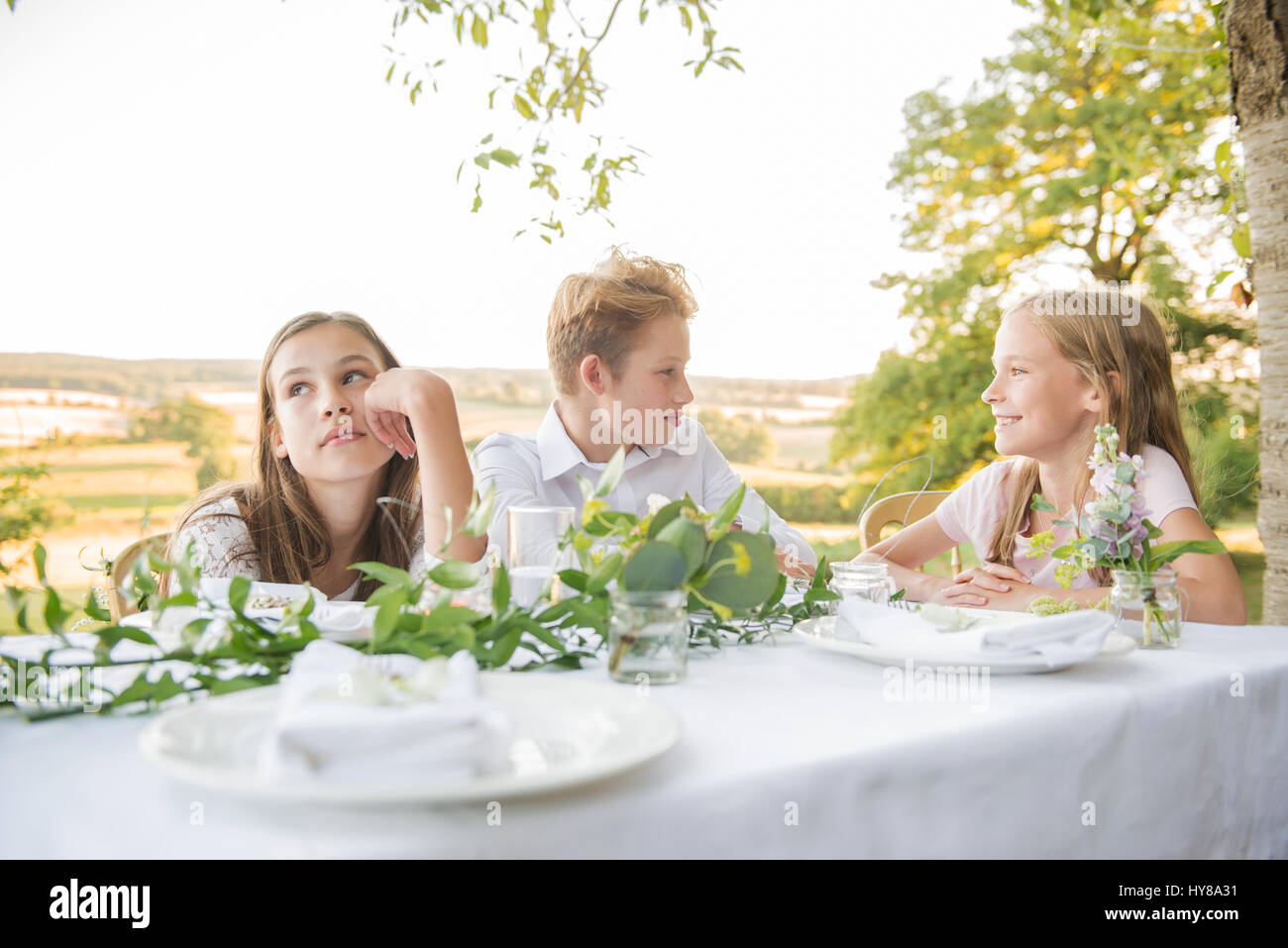 Los niños sentados en la mesa de la cena fuera en el sol Foto de stock