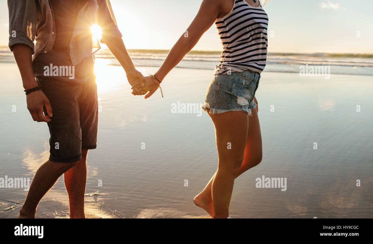 Captura recortada de la joven pareja tomados de la mano y caminar en la playa. Amar al hombre y a la mujer paseando por la orilla del mar. Foto de stock