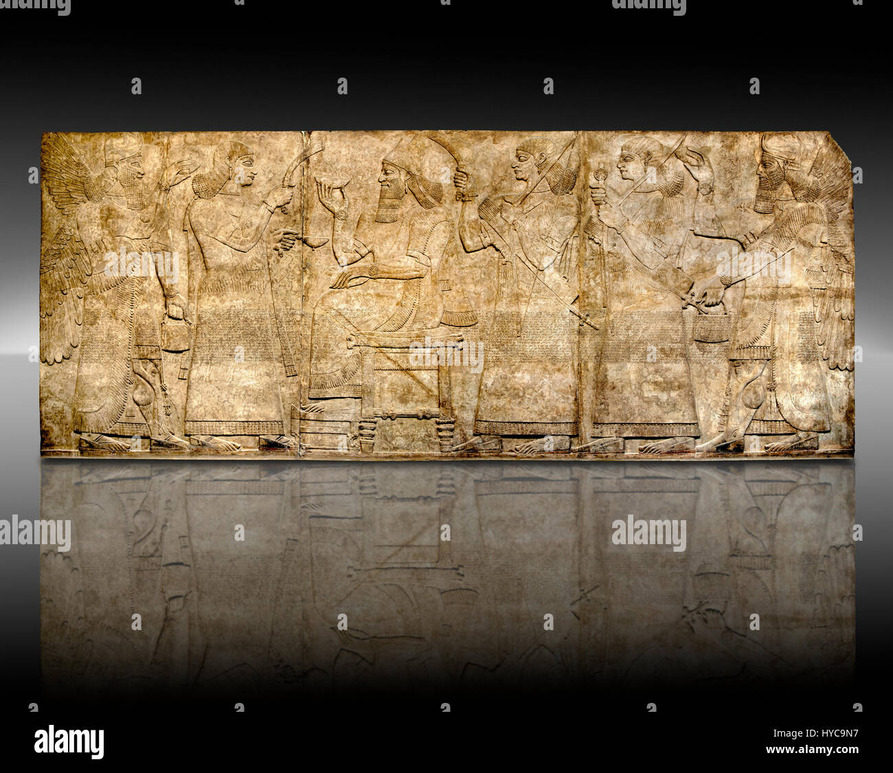 Panel de socorro de la escultura asiria del Rey Ashurnaspiral II entronizado entre dos asistentes. El grupo está flanqueada por espíritus protectores alados. El pan Foto de stock