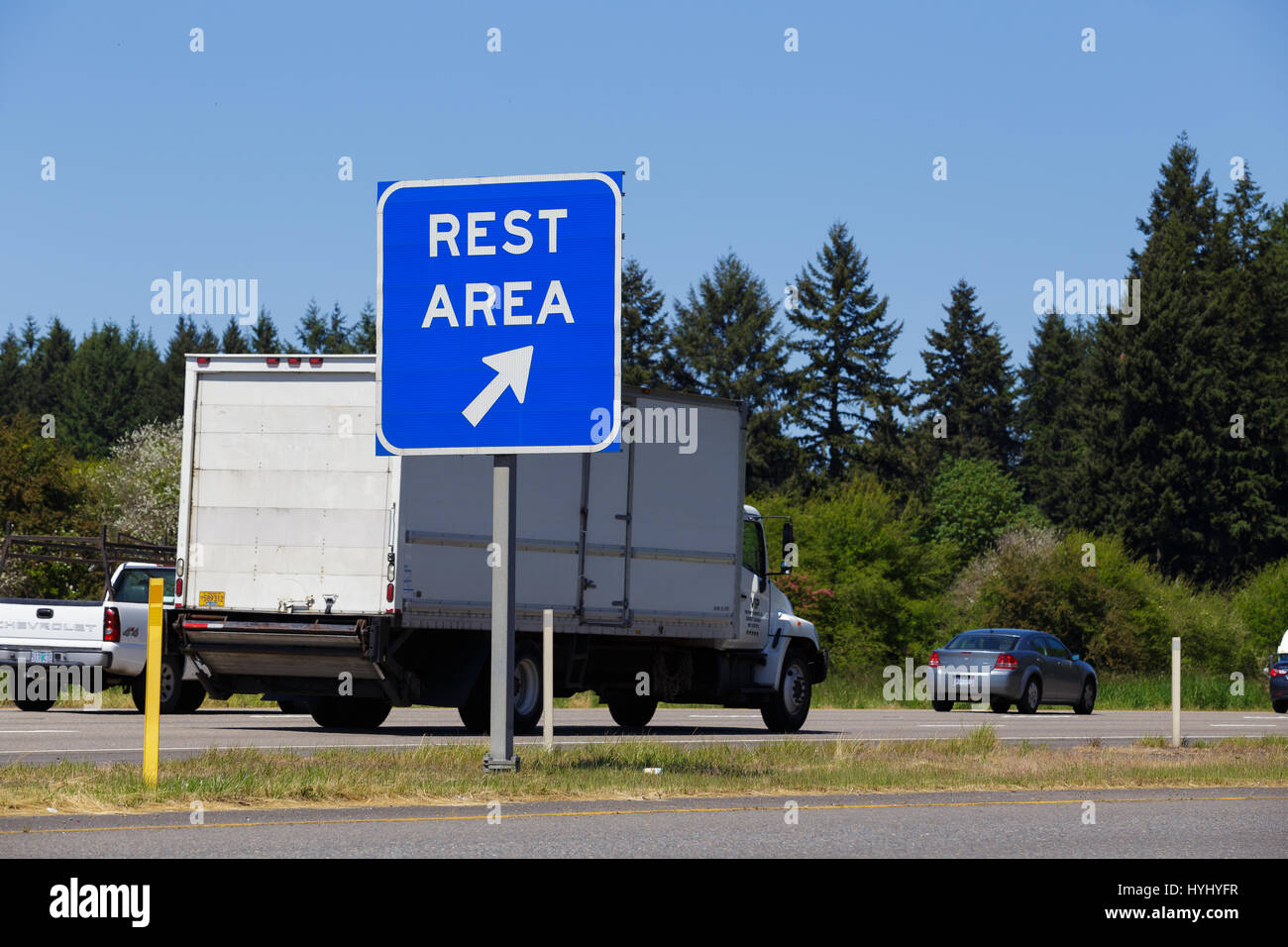 La autopista Interestatal 5, o - Mayo 7, 2015: en azul, área de descanso signo público apuntan a una salida de la carretera con los vehículos que pasan por el fondo. Foto de stock